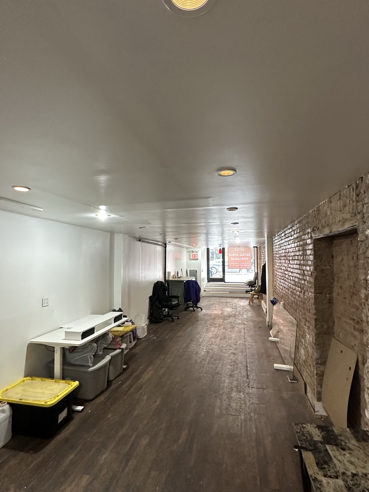 Long interior view of the 84 Clinton Manhattan storefront showing exposed brick, updated flooring, and the front entry.