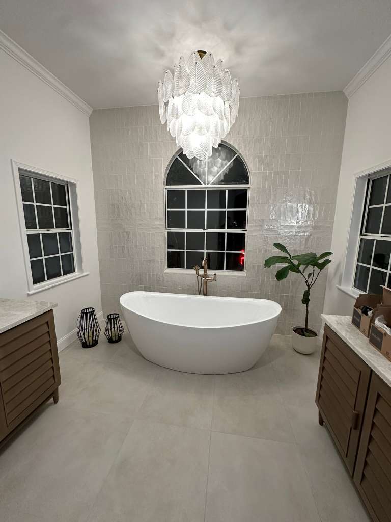 Finished arch-window bath with freestanding tub, twin vanities, and arched focal wall.