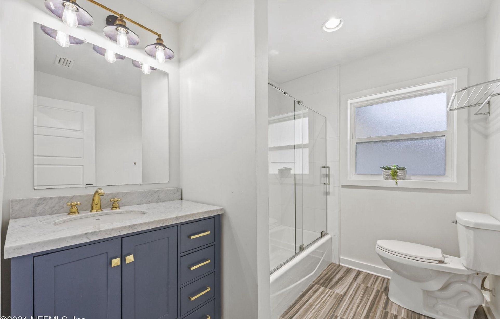 Supporting bathroom with navy vanity, brass fixtures, and marble top.