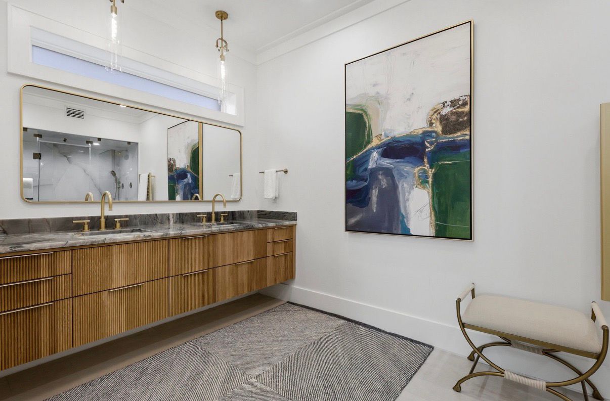 Primary bathroom with double vanity, warm wood detailing, and brass fixtures.