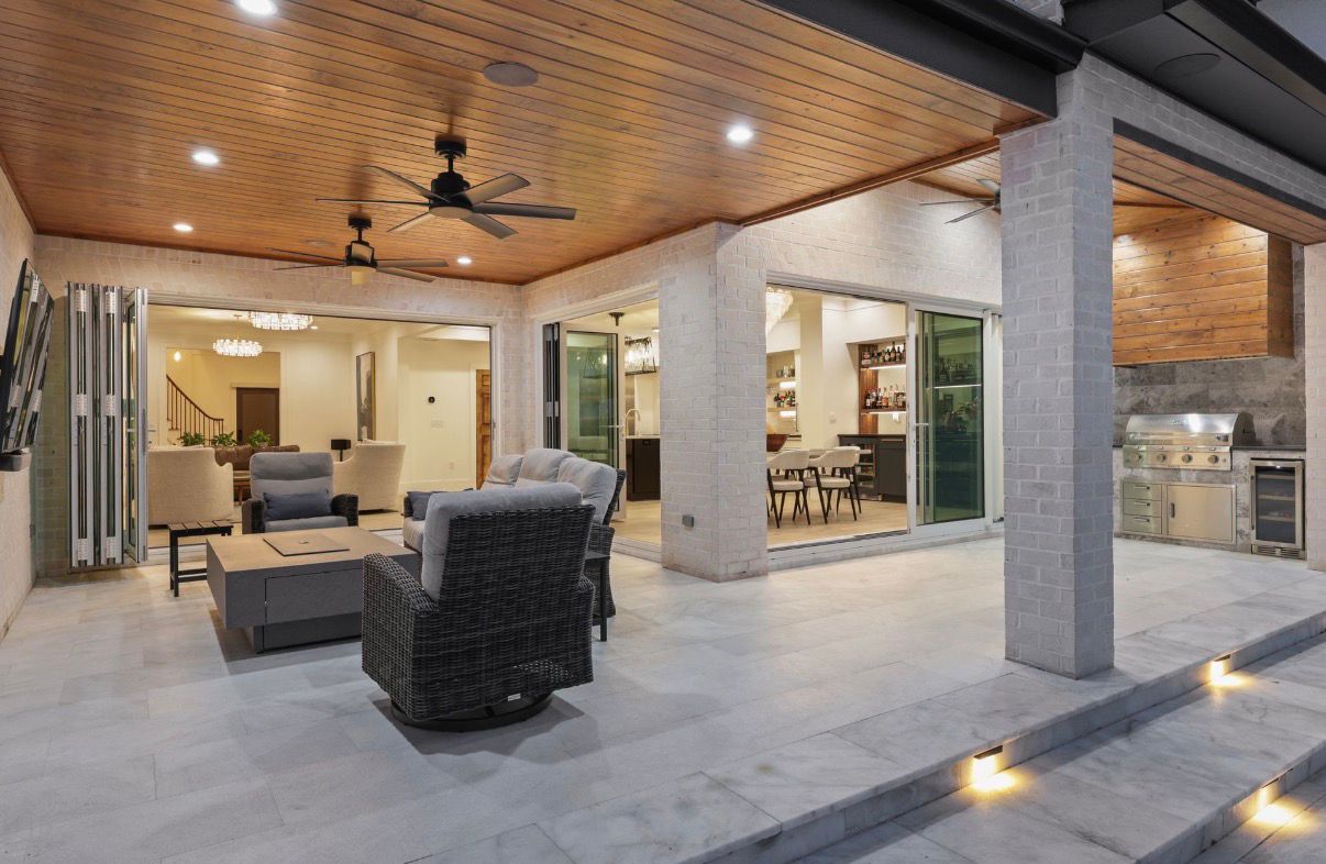 Covered outdoor living area with stone flooring, wood ceiling, and pool deck beyond.
