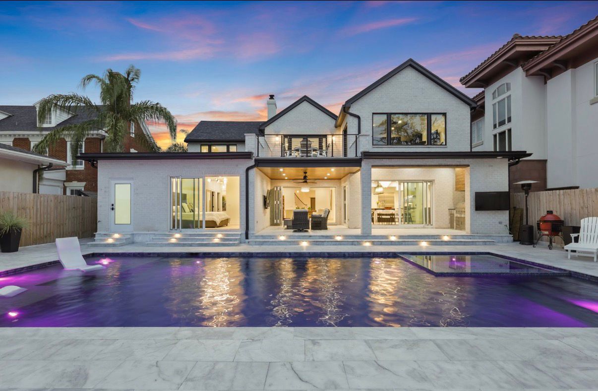 Rear twilight view of a white-brick custom home with illuminated pool and covered outdoor living.
