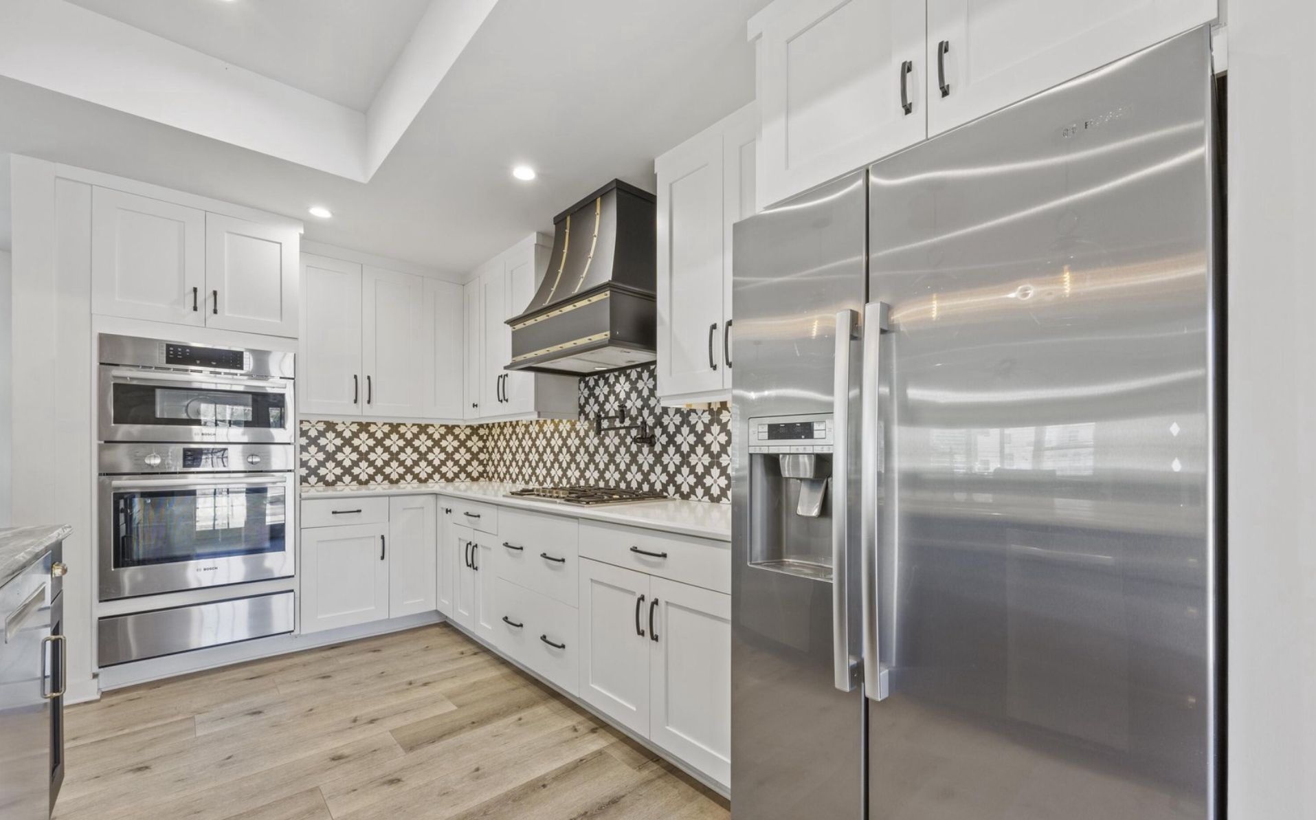 Kitchen corner with stainless appliances, patterned tile backsplash, and white shaker cabinetry.