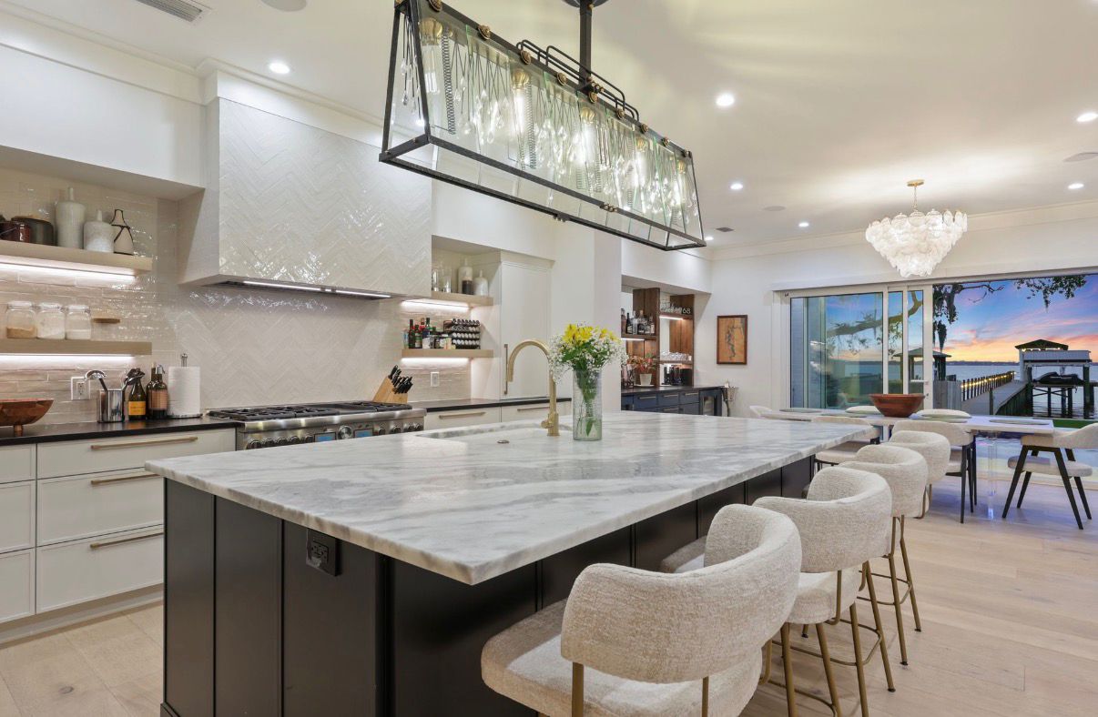 Open waterfront kitchen with dark island, pendant lighting, and evening glow through the windows.