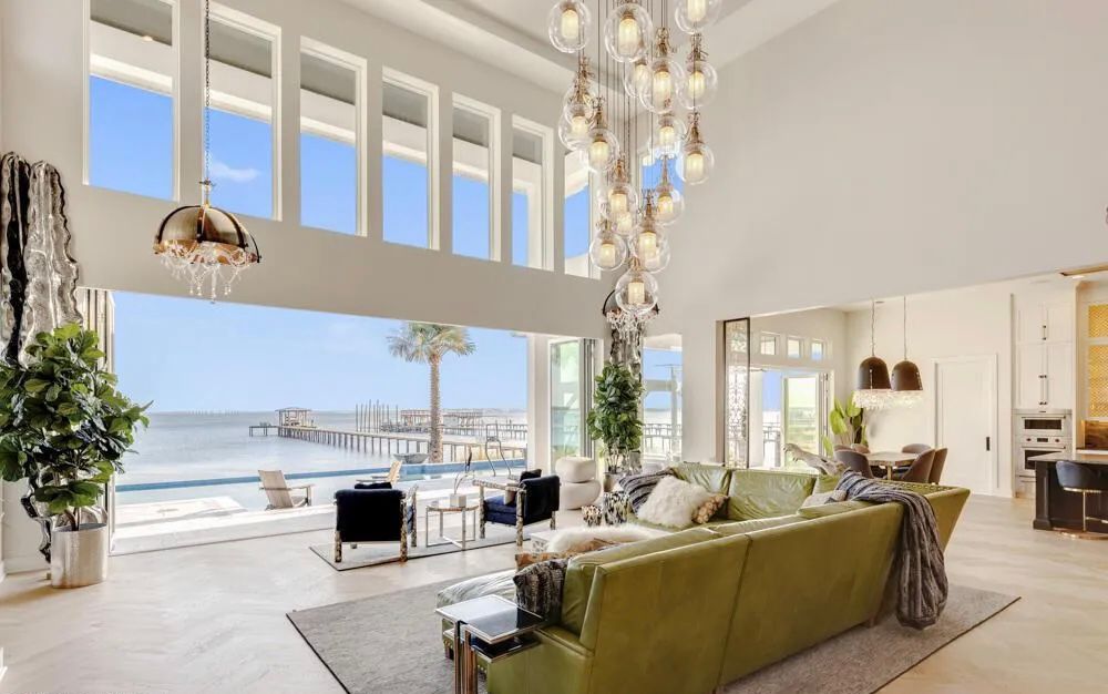 Open great room with tall glazing, sculptural lighting, and view through to the waterfront.