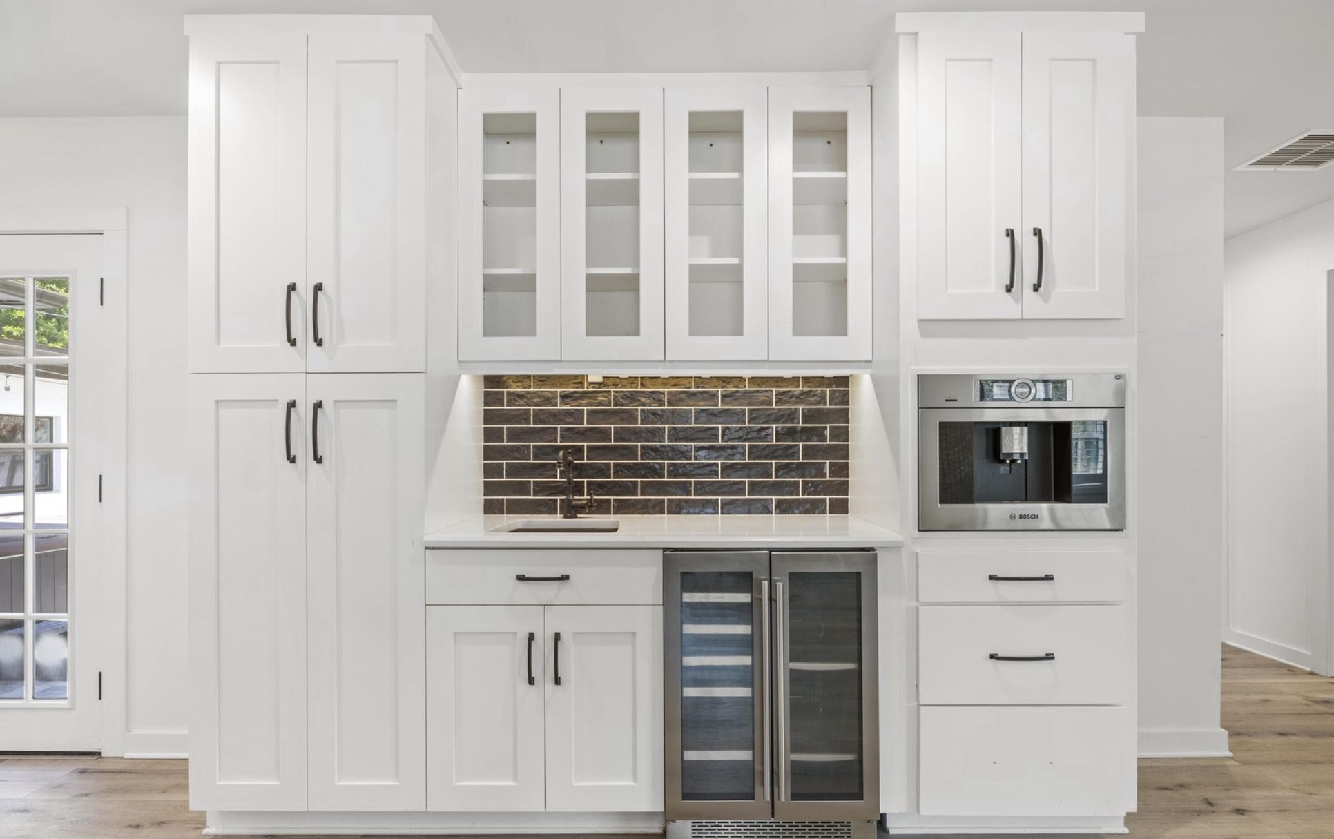 Built-in beverage and wine storage with white cabinetry and dark tile backsplash.