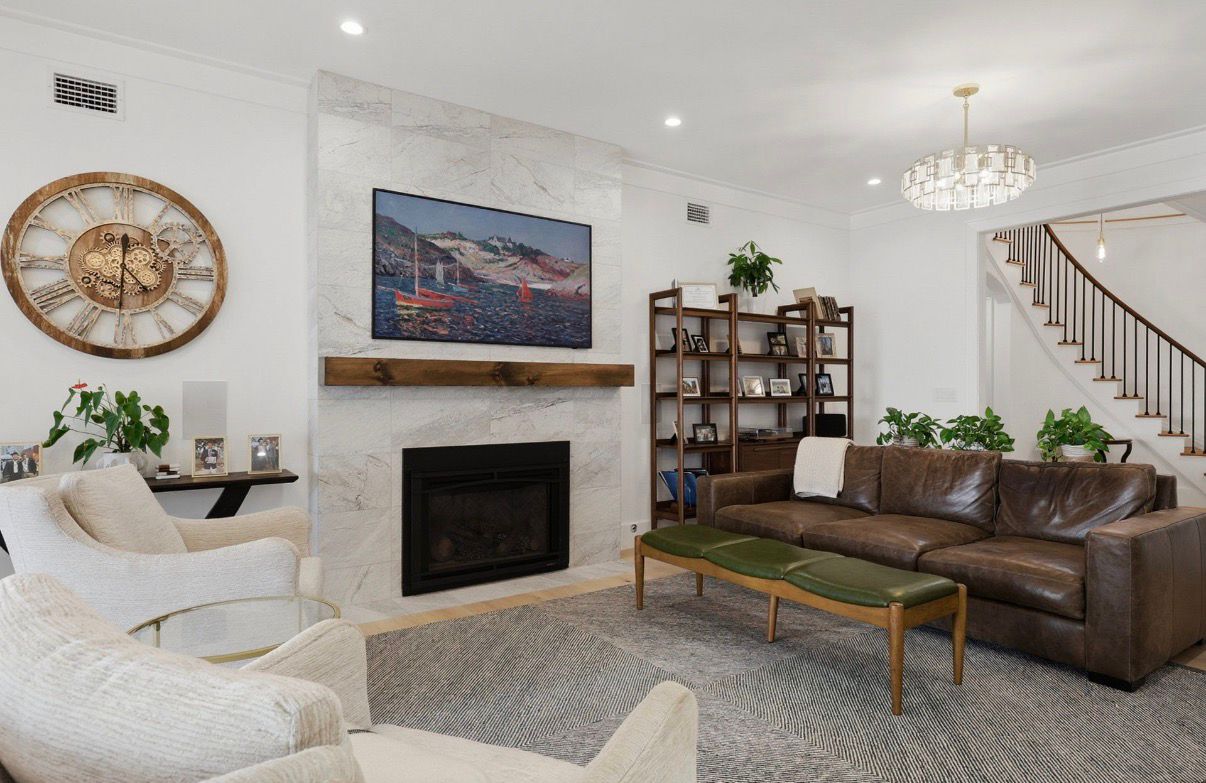 Finished waterfront living room with marble fireplace, leather seating, and warm chandelier lighting.