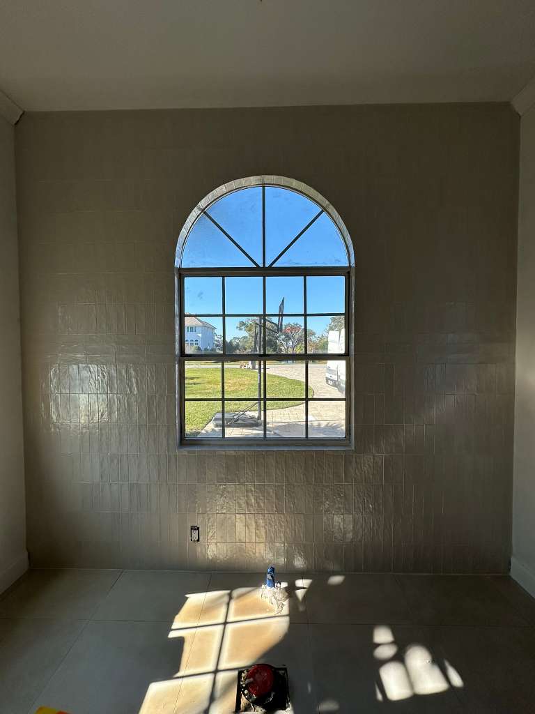Arch-window bathroom during tile installation before fixtures and glass are completed.